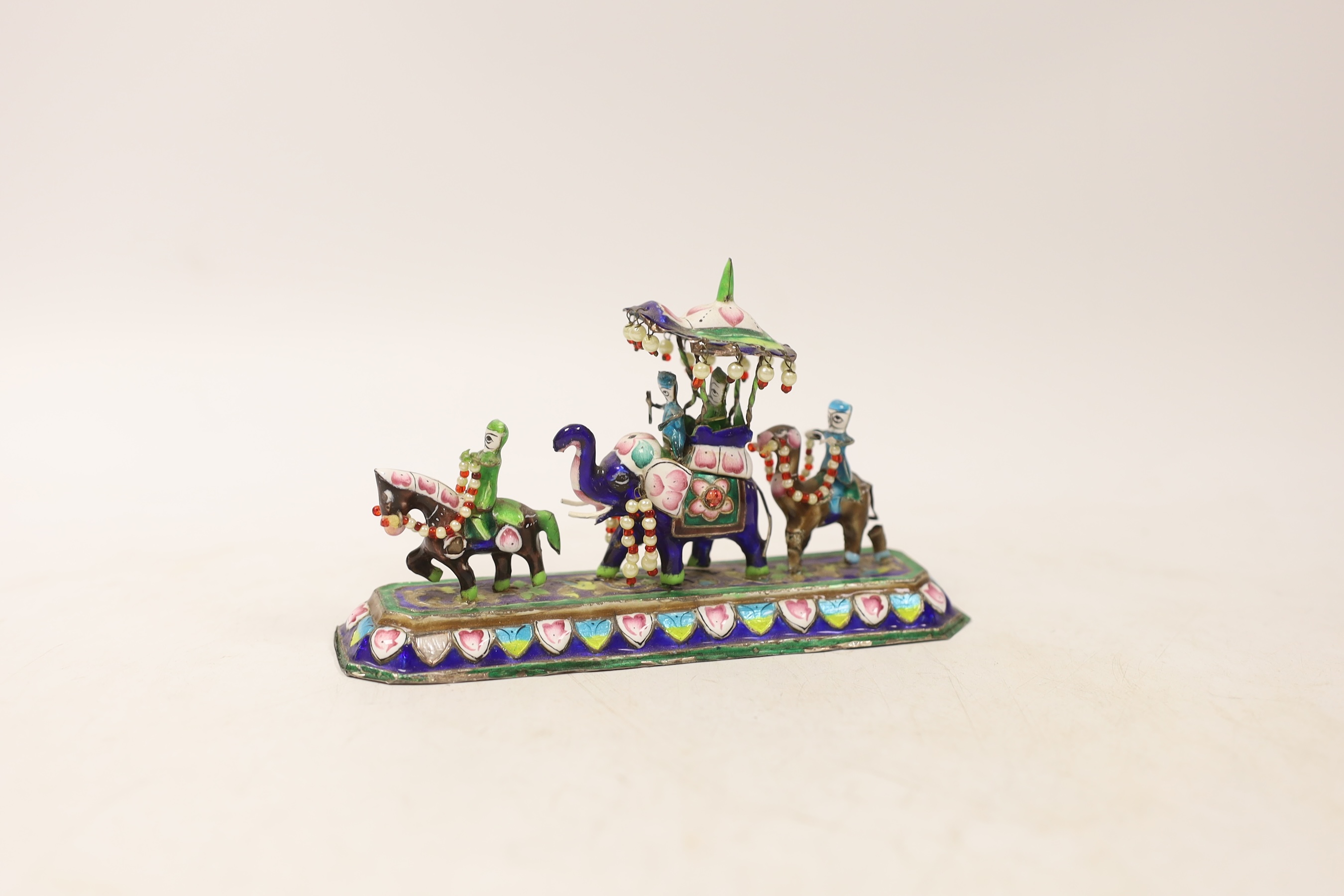 An Indian enamelled white metal model of an elephant parade, with a stamped floral decorated base, stamped ‘silver’, 15cm long. Condition - some enamelling missing or chipped